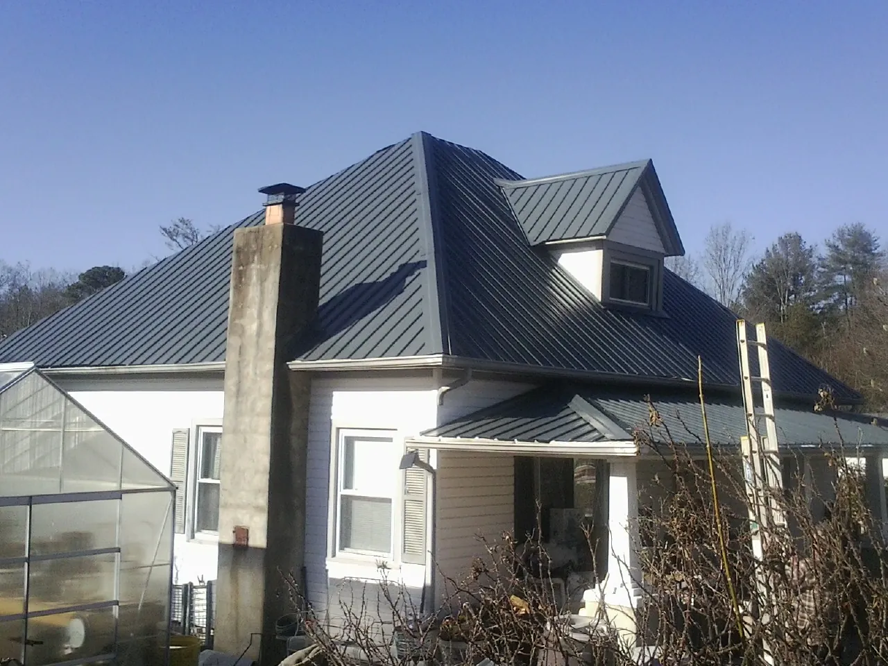 Dark blue standing seam metal roof on a white farmhouse with dormer — Slate & Tile Roof Repair by Roofing Brothers in Mount Savage