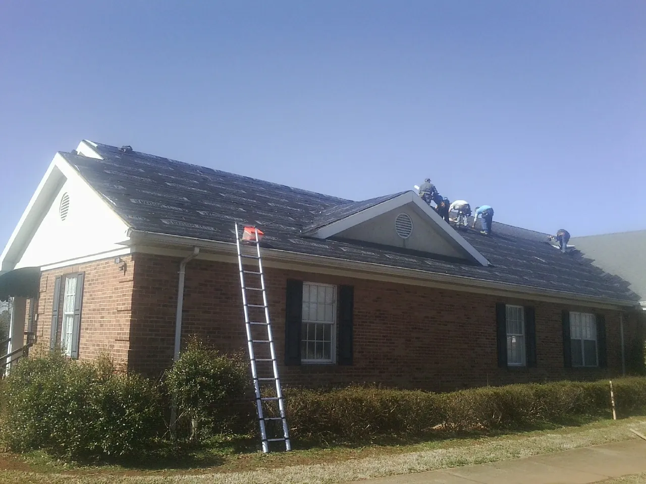 Crew tearing shingles off a brick ranch roof with a ladder set — Metal Roof Repair work by our crew in Mount Savage