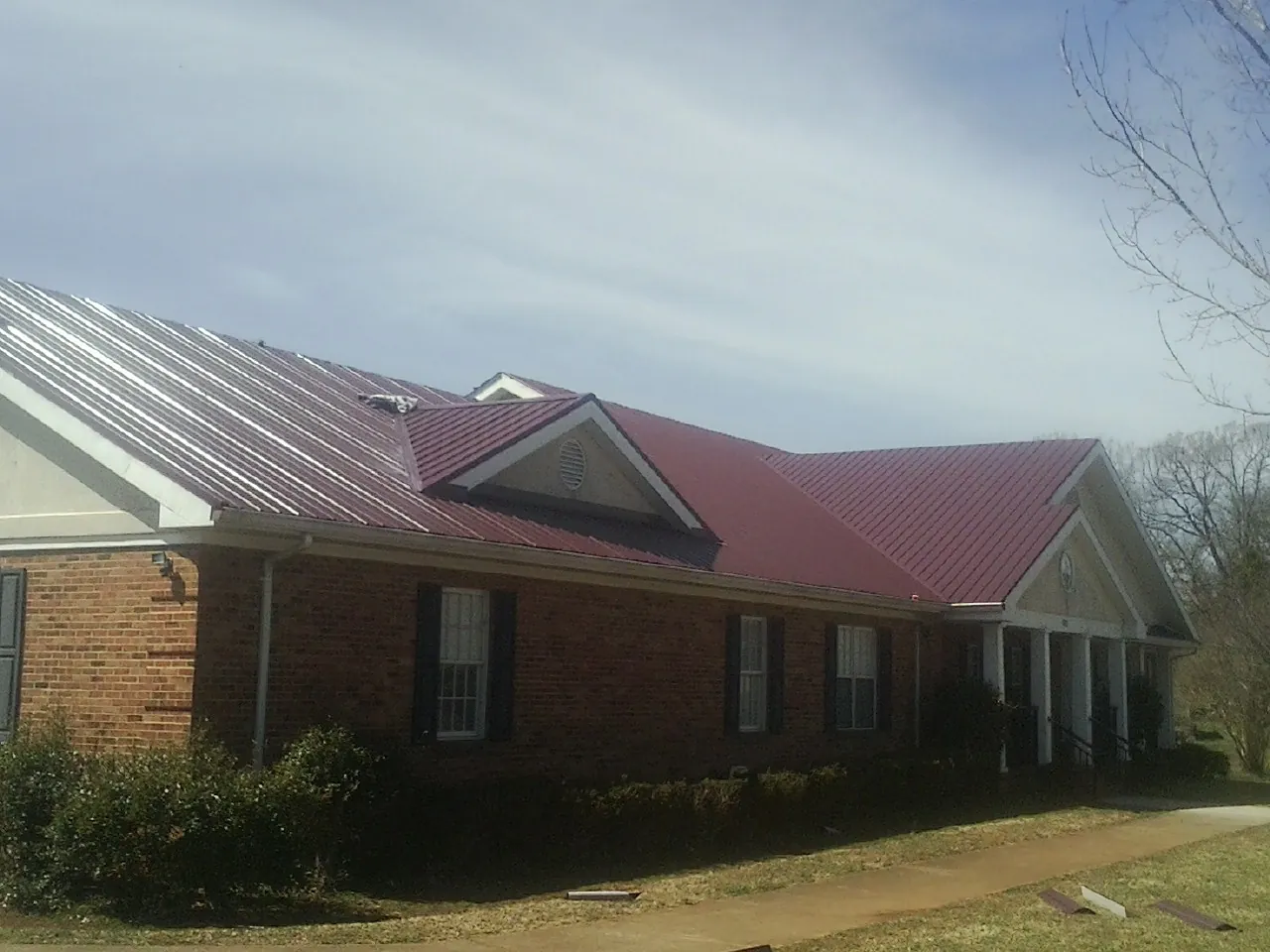 Red metal roof with gabled entries on a long brick building, from a Hail Damage Roof Repair job in Mount Savage