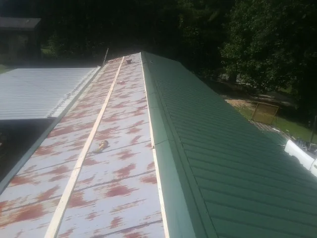Old rusted panels beside newly installed green metal roofing — Wind Damage Roof Repair by Roofing Brothers in Mount Savage