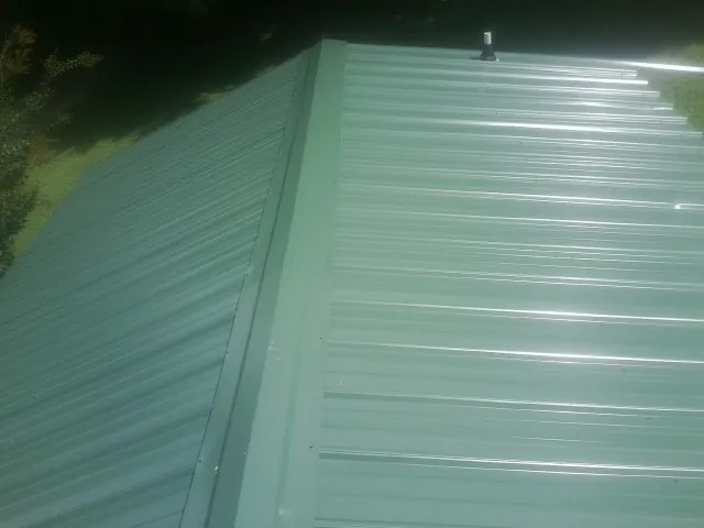 New green metal panels meeting at the ridge of a roof — Flat Roof Repair work by our crew in Mount Savage