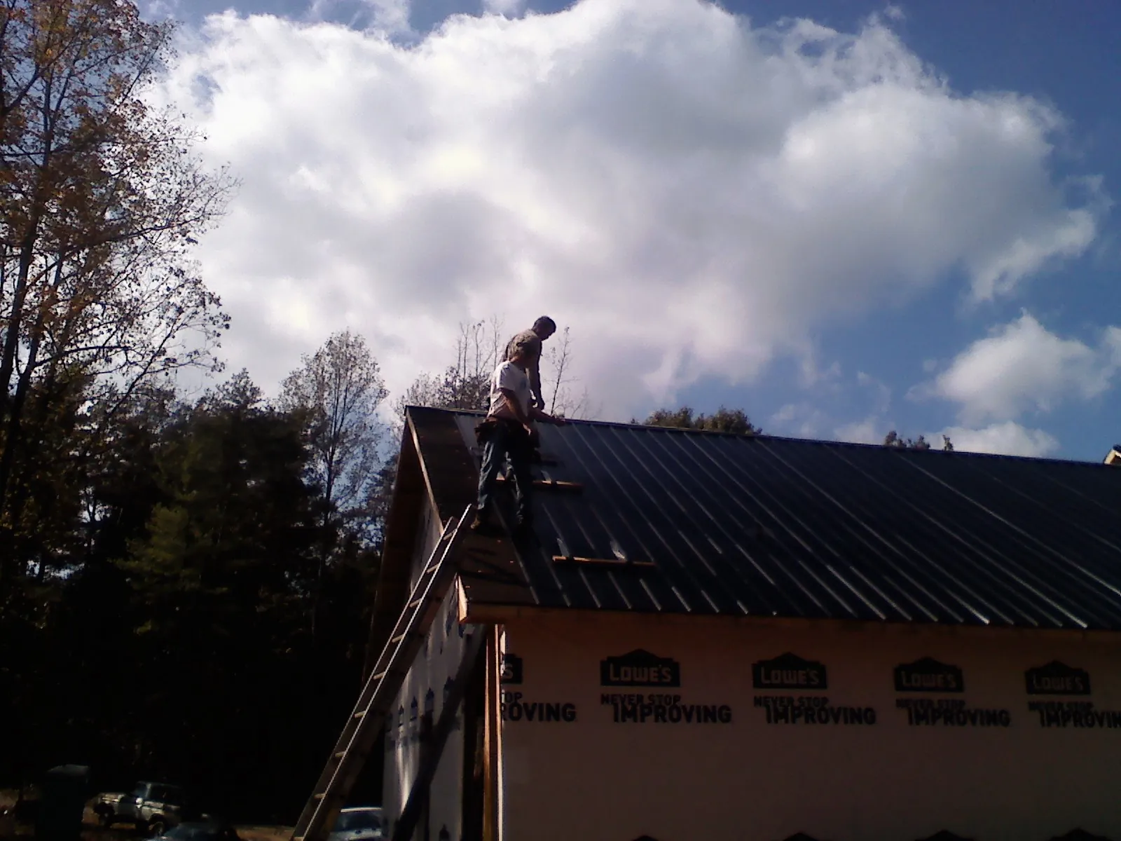 Roofer fastening dark metal panels high against a cloudy sky, from a Roof Inspection job in Mount Savage