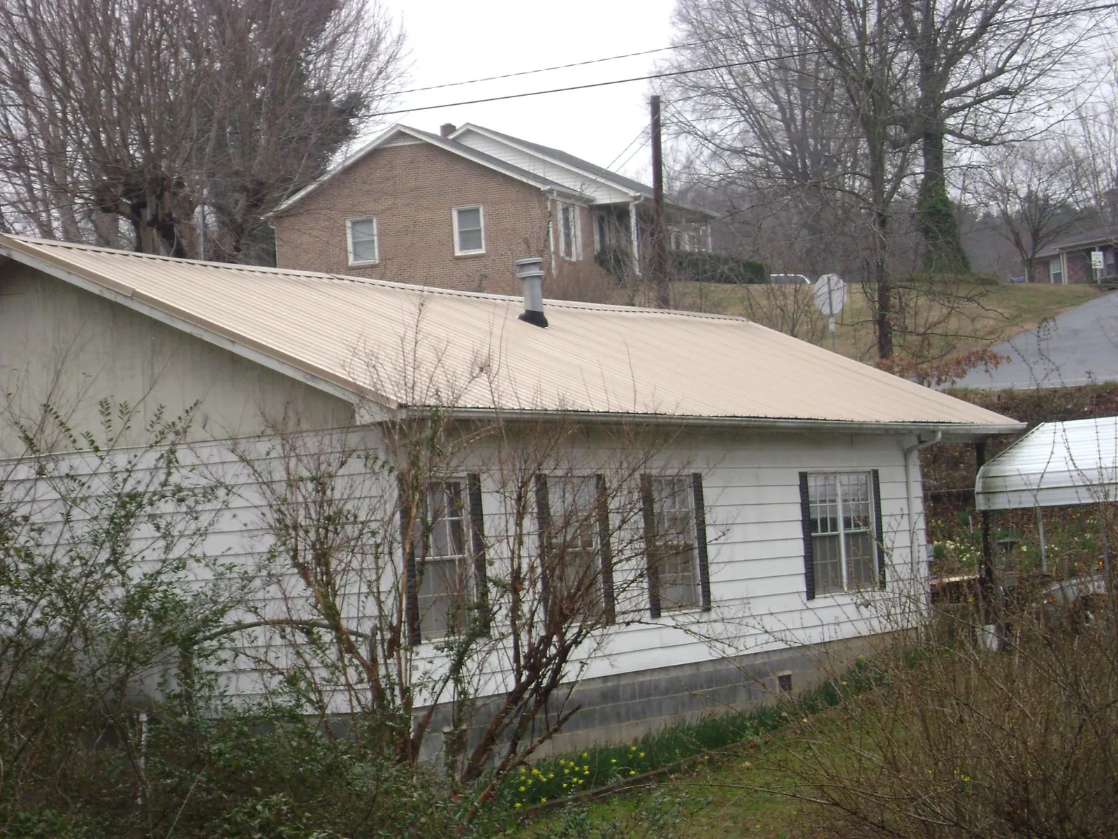 Tan metal roof on a white sided house set into a hillside — Commercial Roofing by Roofing Brothers in Mount Savage